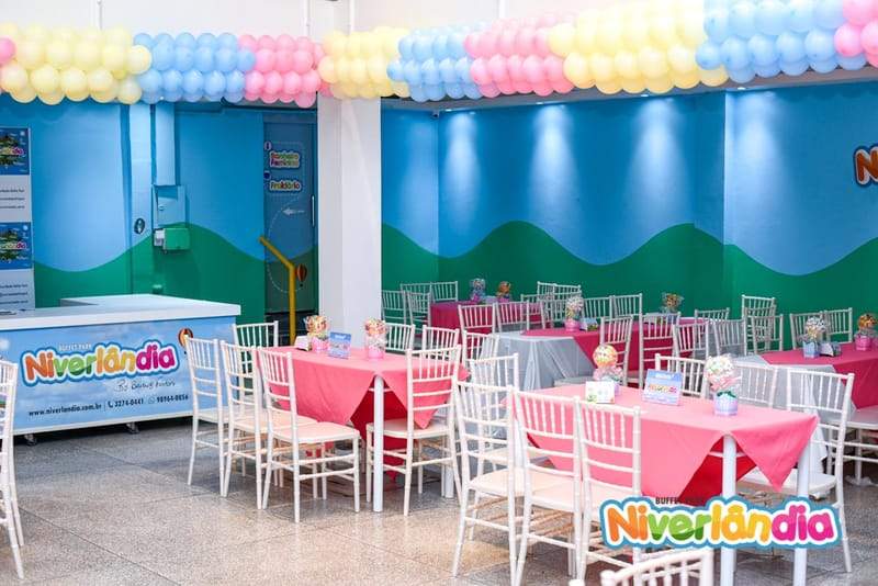 Área do Salão do Niverlândia com mesas, cadeiras e decoração colorida
